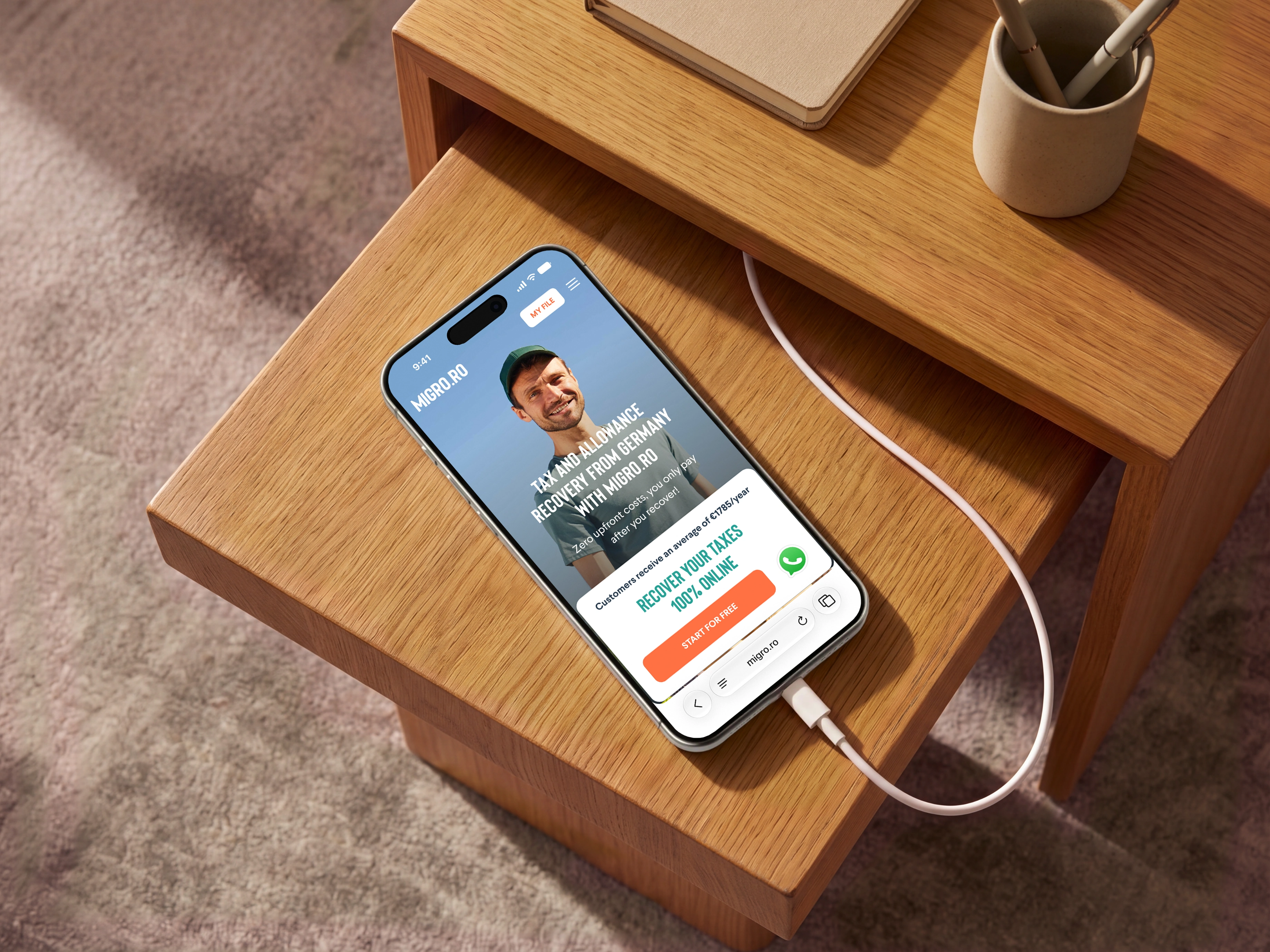 Migro’s tax recovery website on a phone resting on a wooden table, with Frank and a clear application button